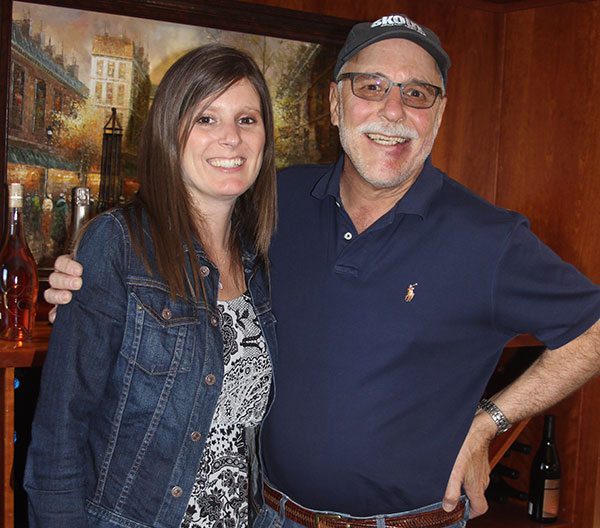 Father and daughter pose in front of wine bottles and painting