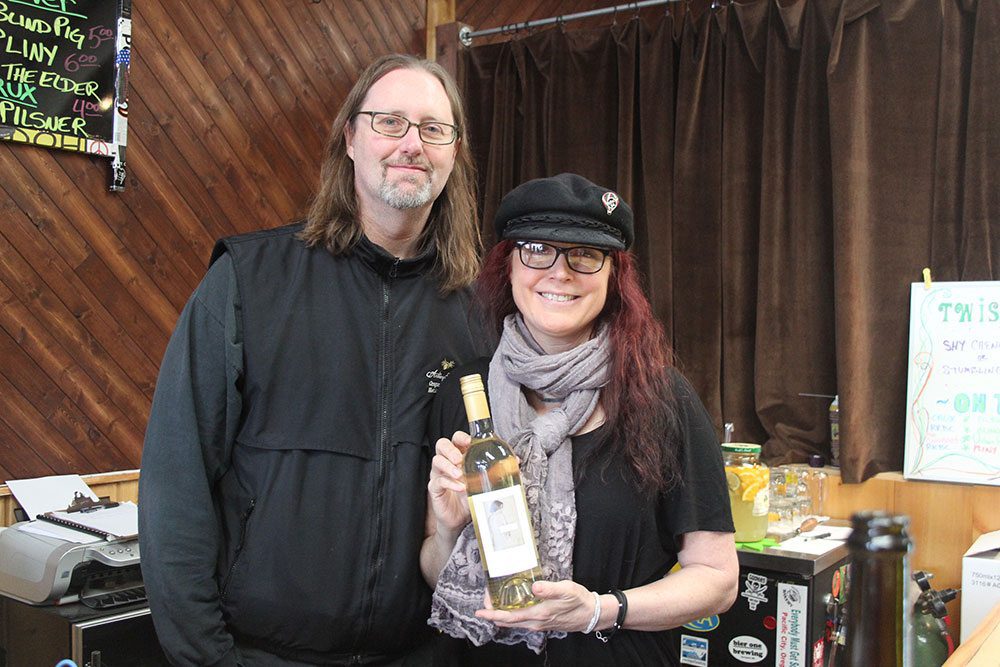 Man and woman both wearing glasses show off bottle of white wine